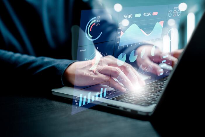 Person using a laptop with digital charts, graphs, and data visualizations overlaid on the screen.